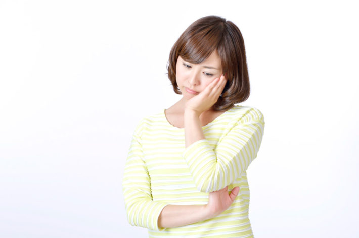 ボーダーシャツを着た女性が手を頬にあて悩んでいる画像