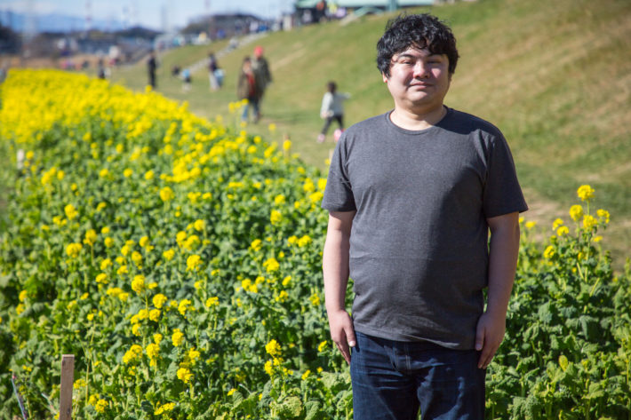 花畑をバックに立ち、微笑んでいる太った男性