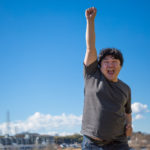 空に拳を掲げシャウトしている太った男性