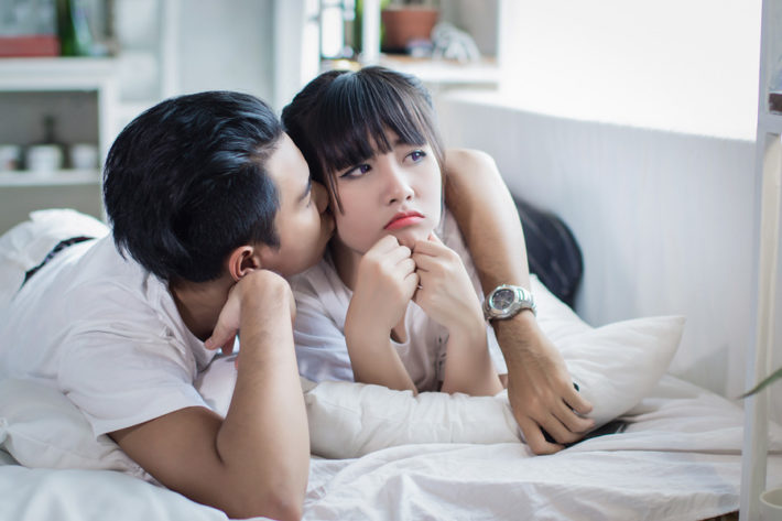 不機嫌そうに窓の外を眺める女性の頬にキスする男性