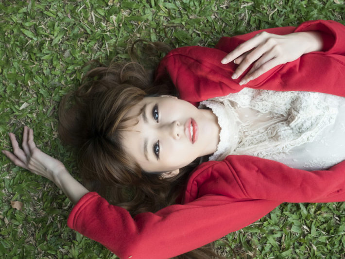赤いカーディガンを着た女性が芝生に仰向け寝ている画像