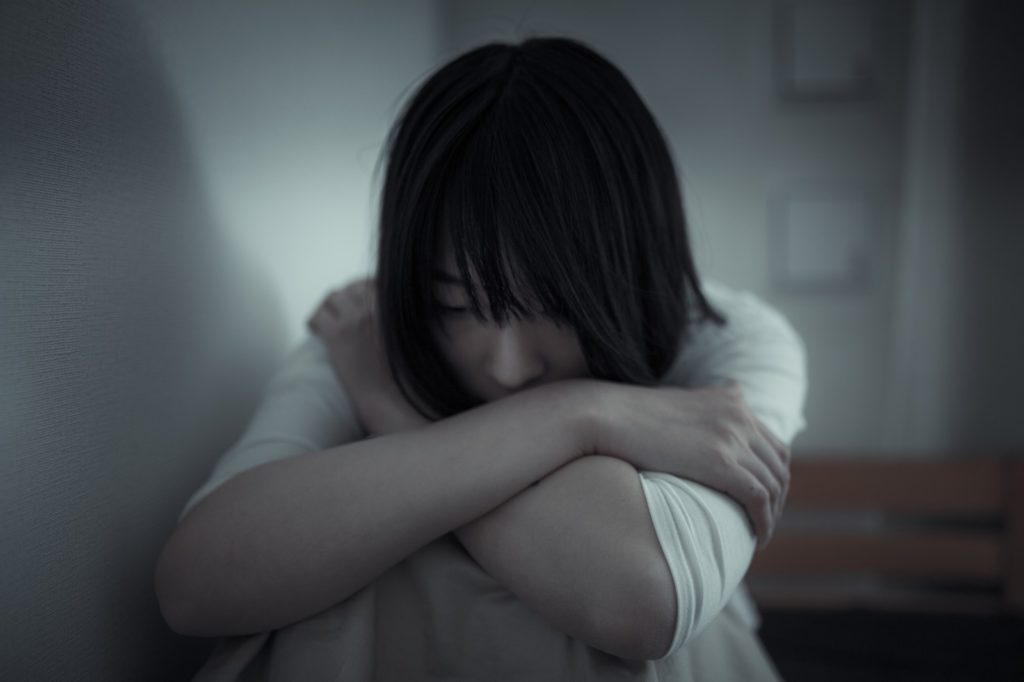 ベッドの上で膝を抱えて考え込んでいる女性