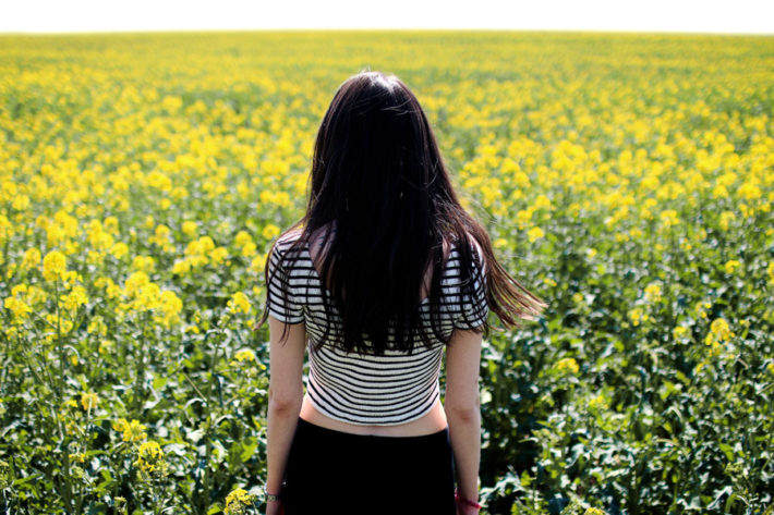 菜の花畑を見つめている女性の後ろ姿