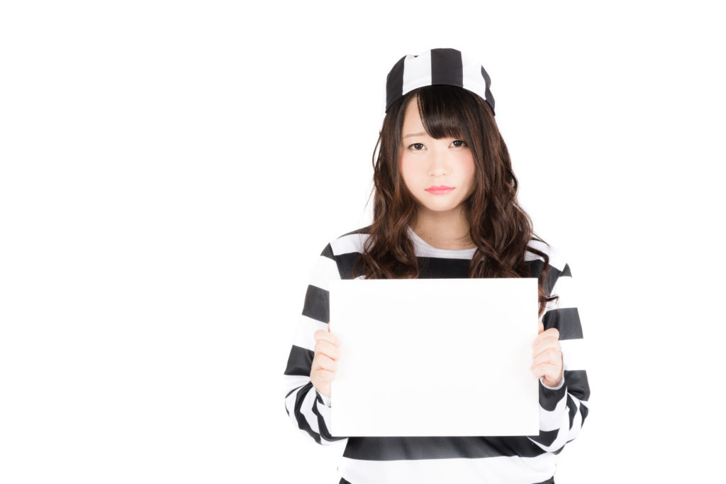 囚人服のコスプレをした女性が真っ白な保ワイドボードを出している画像
