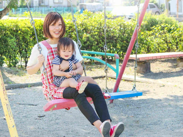 子供を膝に乗せてブランコしている保育士女性