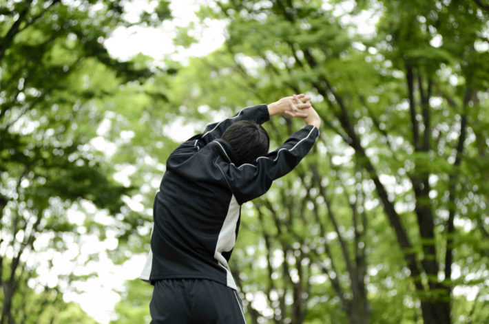 森の中でストレッチしている男性の後ろ姿