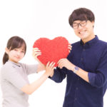 男女のカップルがハートのクッションを持っている画像