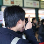 人並みを撮影しているオタク男性、後ろ姿