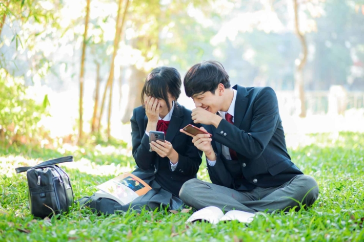 芝生の上に座り仲良く話している高校生の男女