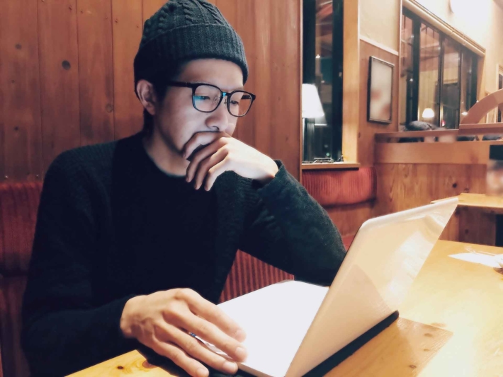 カフェでMacbookを操作しているニット帽でメガネの男性