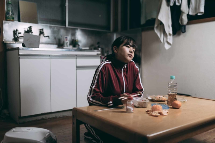 ボロアパートのリビングでジャージ姿でぼーっとしている女性