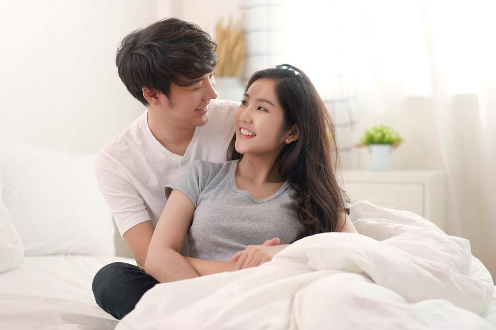ベッドに座る女性を後ろから抱きしめている男性